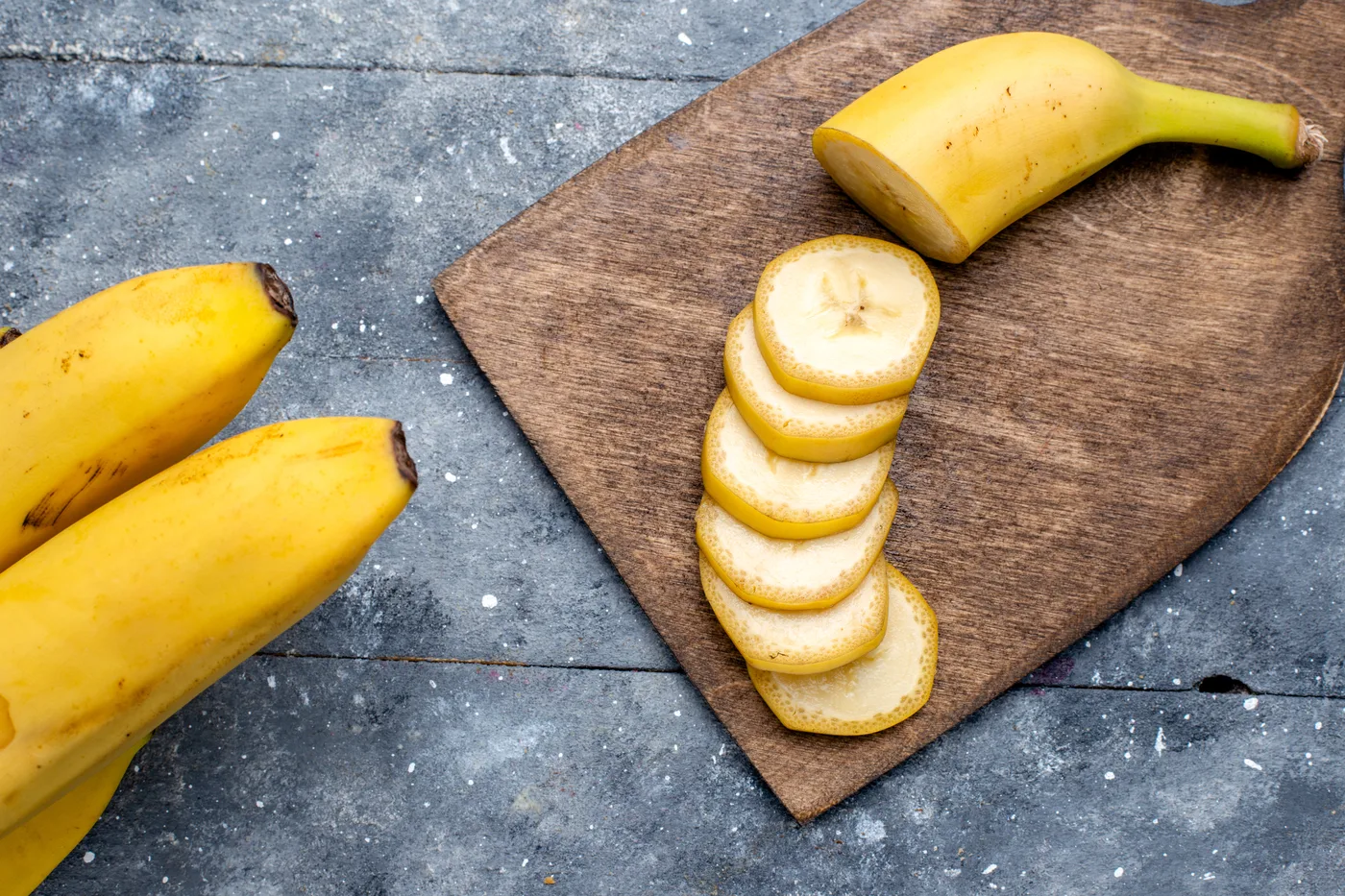 Banan pokrojony w plastry obok całych bananów na desce