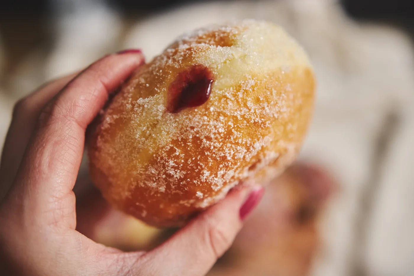 Dłoń trzyma pączka z nadzieniem obsypanego cukrem