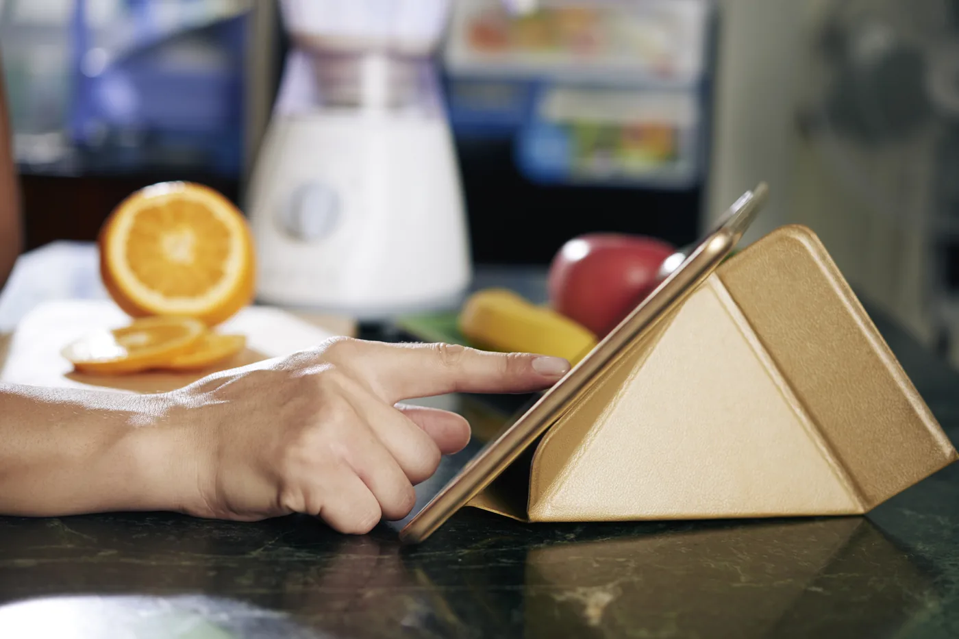 Dłonie przeglądają tablet na kuchennym blacie, obok owoce